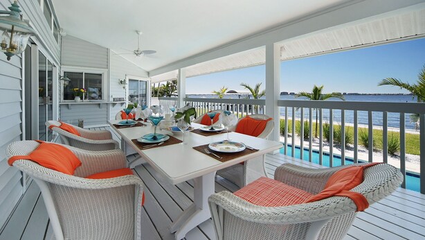 A covered outdoor dining area with wicker chairs and a table set for two, overlooking a pool and beach. - Villa Southern Living, dreamy waterfront vacation home in Cape Coral (Cape Coral)