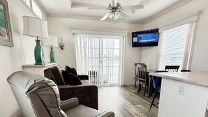 A living room with a sofa, a ceiling fan, a TV, and a dining area with a table and chairs. - Central located cozy cabin with resort amenities (Naples)