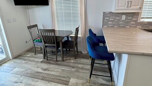 A modern kitchen with white cabinets, a wooden floor, a dining area with chairs, and a flat-screen TV mounted on the wall. - Central located cozy cabin with resort amenities (Naples)