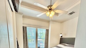 A bedroom with a bed, a ceiling fan, a window with curtains, and a door. - Central located cozy cabin with resort amenities (Naples)