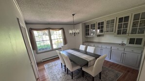 A dining area with a table, chairs, a rug, and a kitchen with cabinets and a window.