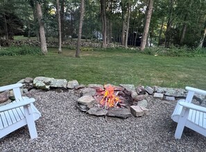 A fire pit surrounded by rocks and gravel, with white benches on either side. - Wonderful 4-bedroom house in Kingston perfect for families.. (South Kingstown)