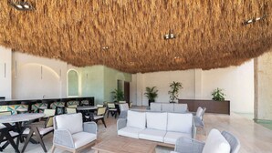 A modern lounge area with a thatched ceiling, wicker furniture, and a seating arrangement. - Maria Tulum - Modern 2BR Retreat with Pool (Tulum)