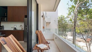 A balcony with wooden chairs, a table, and a view of a garden and building. - Maria Tulum - Modern 2BR Retreat with Pool (Tulum)