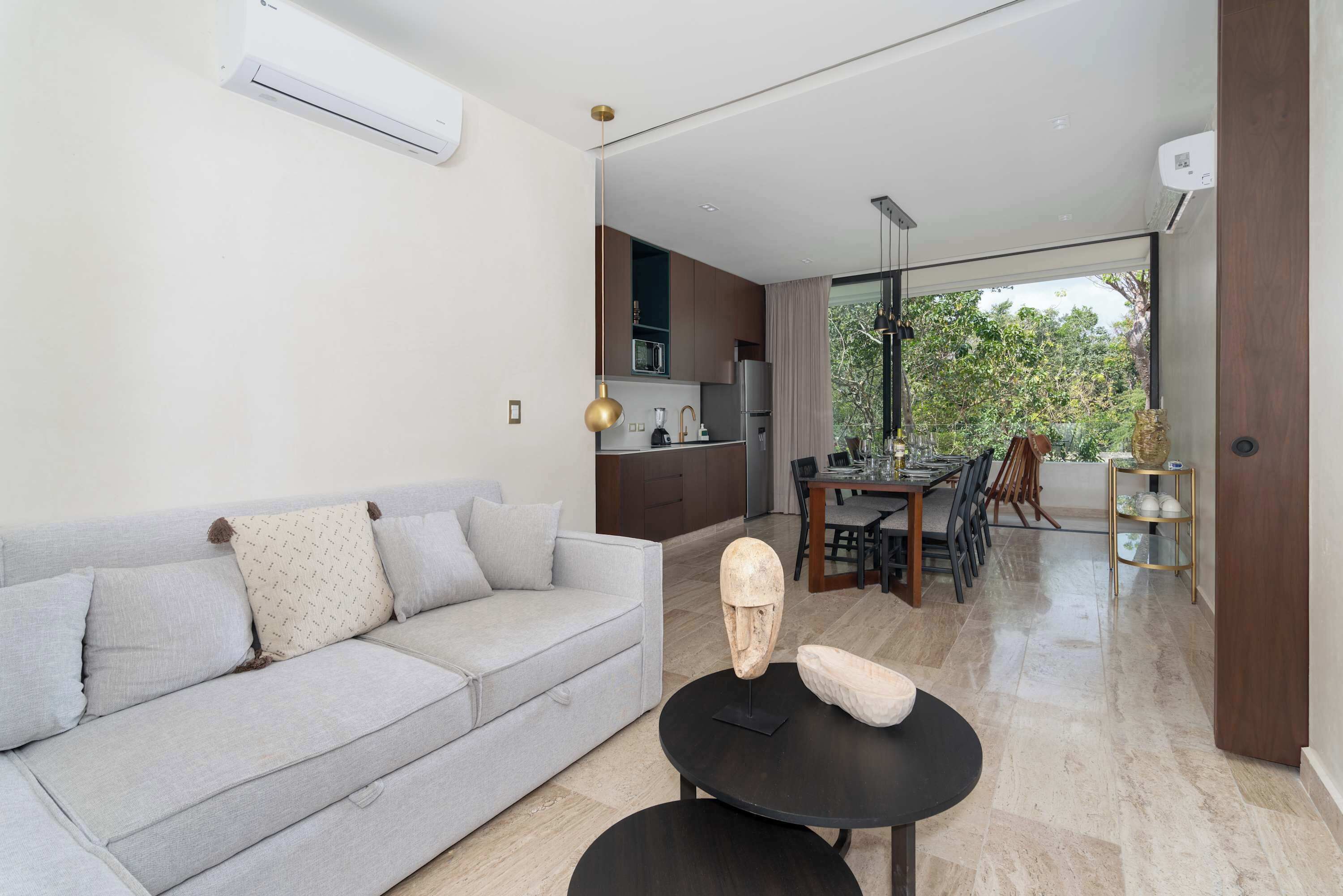 A modern living room with a sofa, a dining table, and a kitchen in the background.