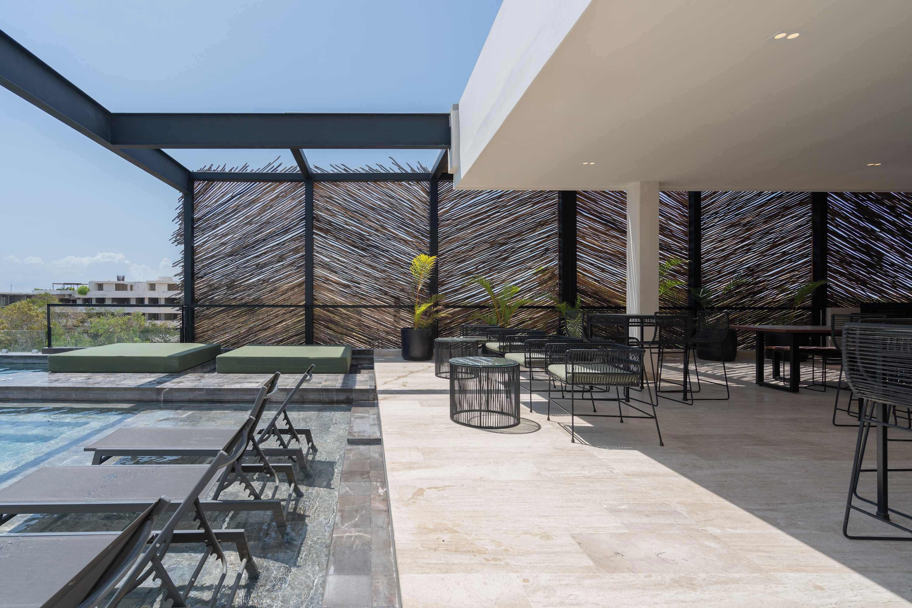 A rooftop pool area with lounge chairs, a table, and a pergola structure.