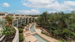 Een modern hotel met een zwembad, omgeven door weelderige begroeiing en een heldere lucht.
