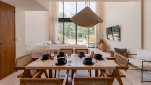 Een eetruimte met een houten tafel gedekt voor zes personen, omringd door rieten stoelen, met een groot raam en uitzicht op groen.