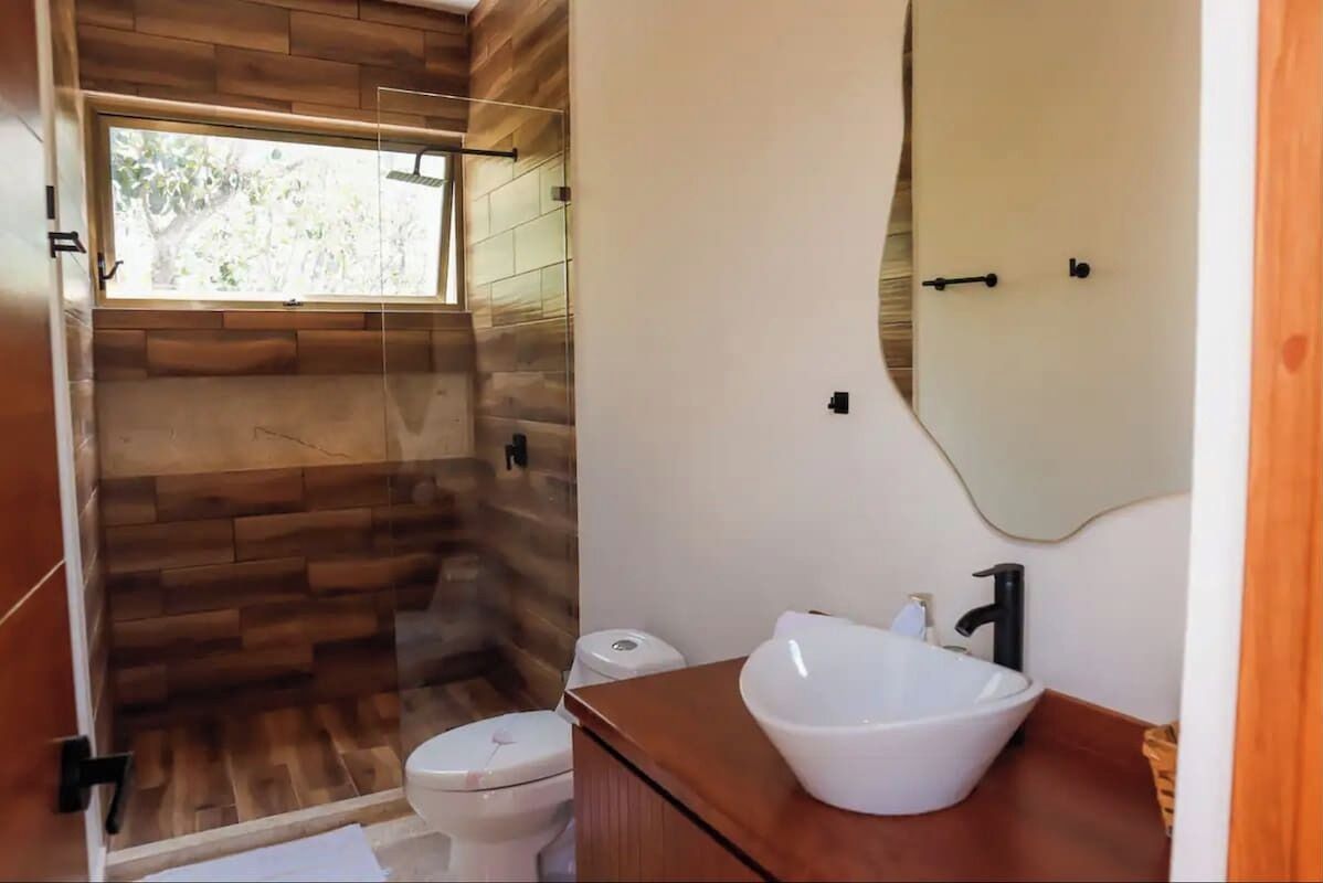 Ein Badezimmer mit Holzboden, einer Duschkabine aus Glas, einer weißen Toilette und einem weißen Waschbecken mit Spiegel darüber.