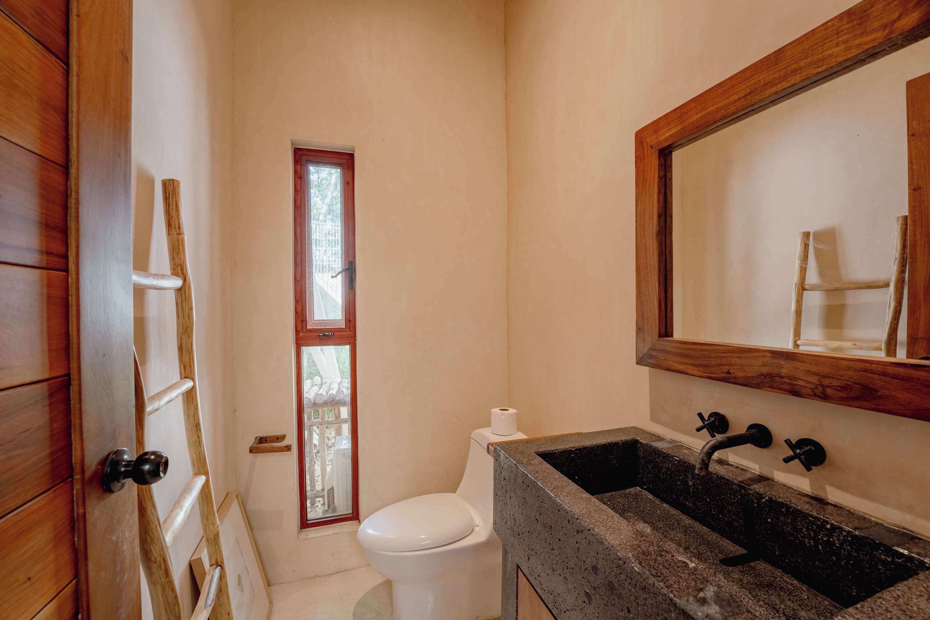 A bathroom with a wooden door, a white toilet, a sink with a dark countertop, and a mirror above the sink.