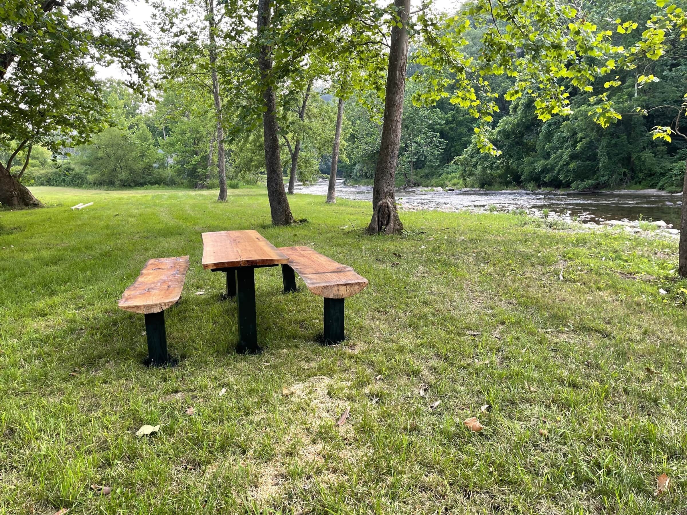 A picnic table in a grassy area with trees and a river in the background.