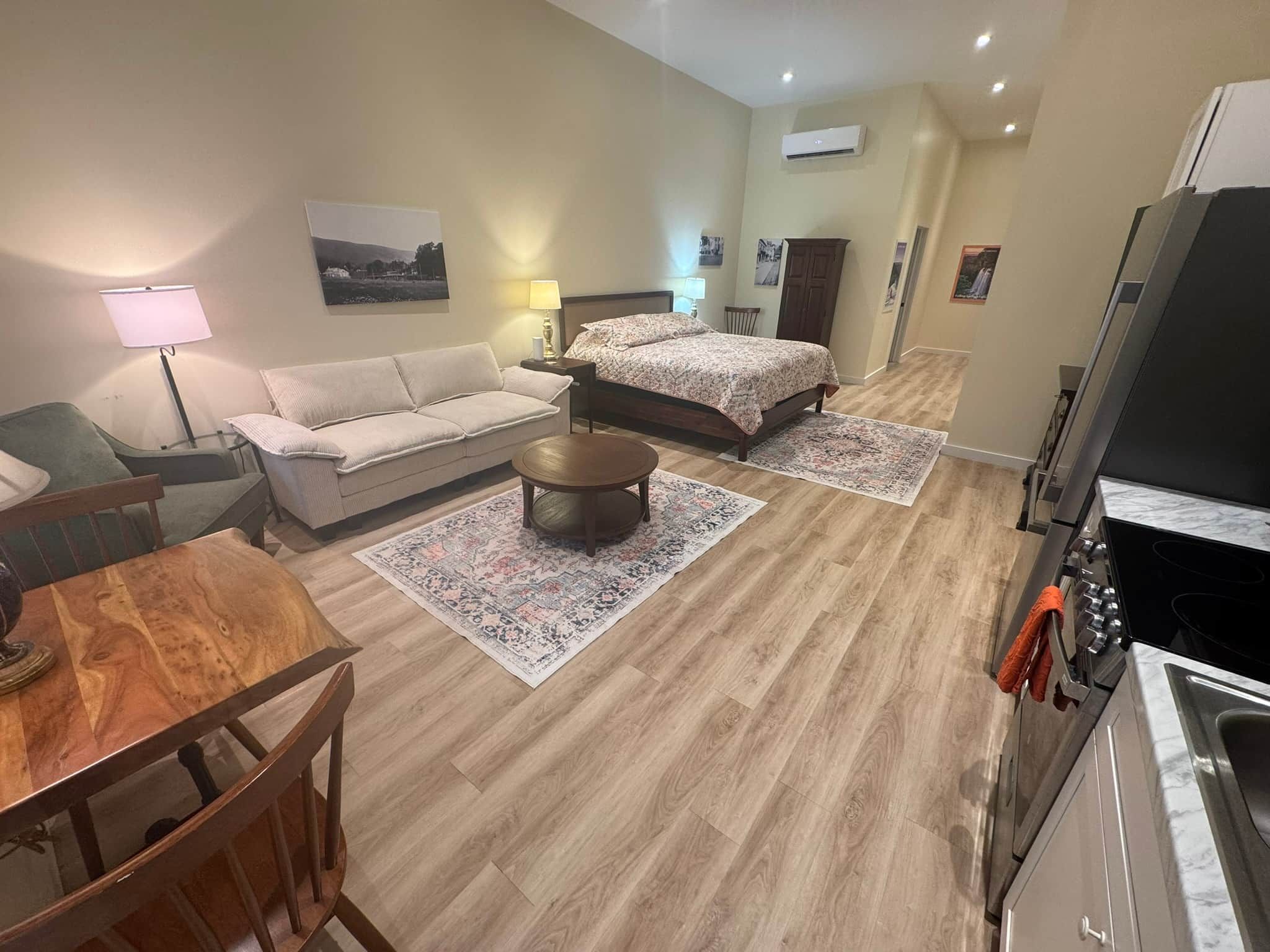 A modern hotel room with a sofa, a bed, a dining table, and a kitchen area.
