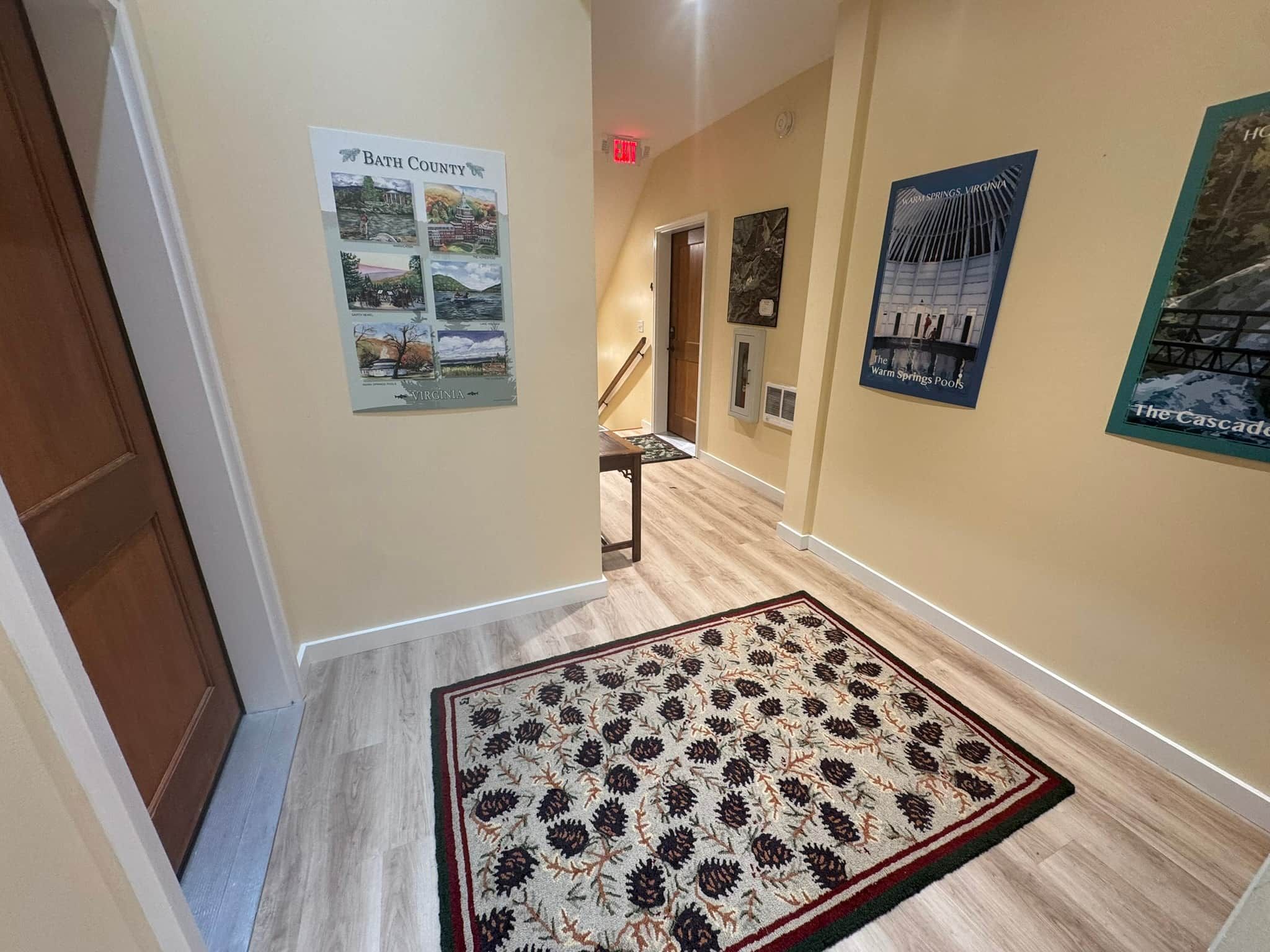 A hallway with a wooden floor, a patterned rug, and several posters on the walls.