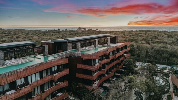 Hotel de diverses plantes amb piscina sense aresta a la terrassa, vista a l'oceà i paisatge desert a la part posterior.