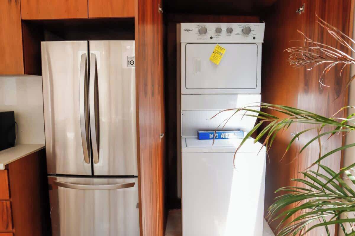 Une cuisine compacte avec un réfrigérateur en acier inoxydable, un lave-linge blanc et une boîte bleue posée sur le plan de travail.