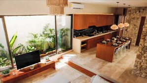 A modern living space with a TV, seating area, kitchen, and dining area with a stone accent wall. - Huge 10BR Luxury Villa Complex w/ 6 Private Pool (Tulum)