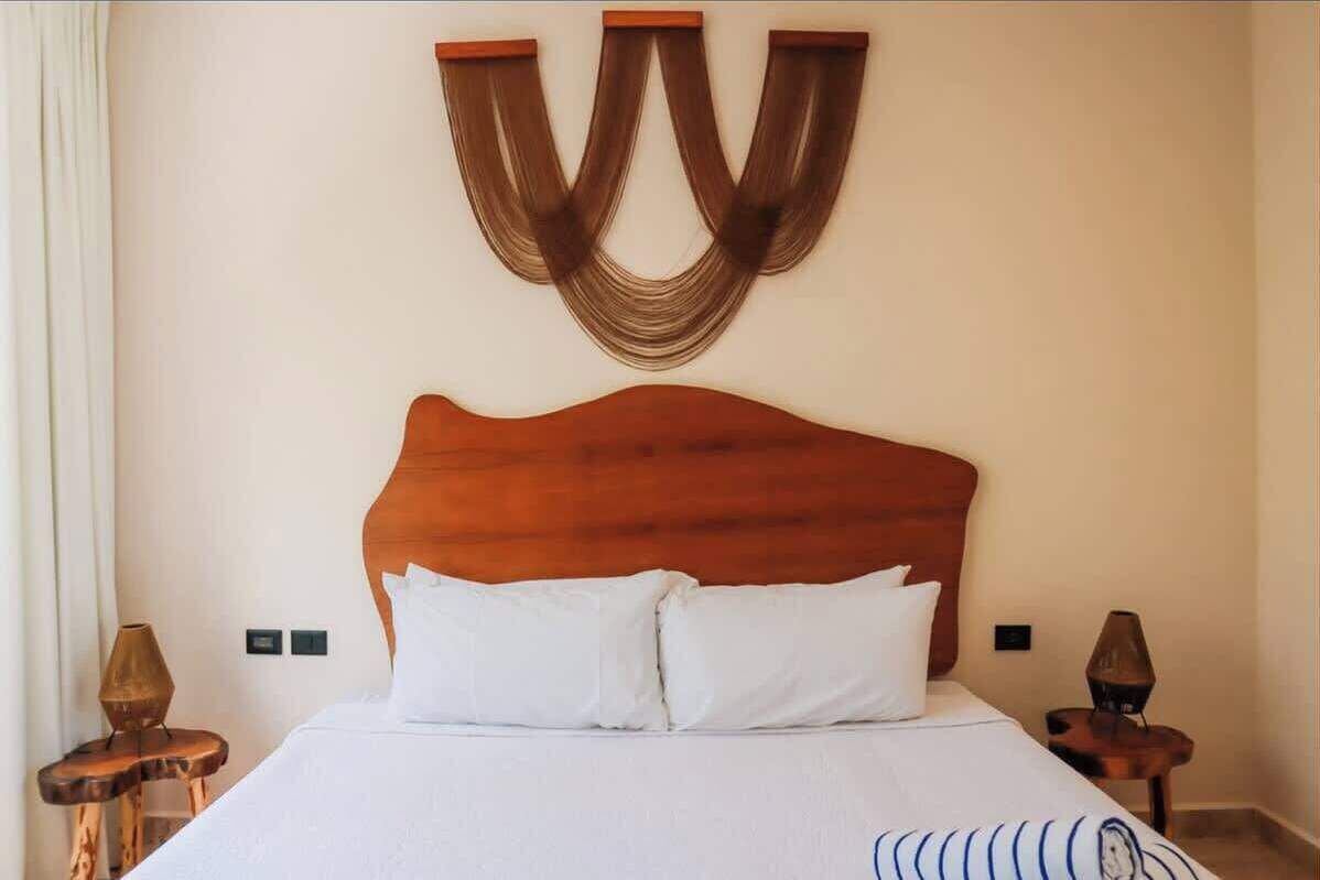 Ein Hotelzimmer mit einem hölzernen Kopfteil, einem Bett mit weißer Bettwäsche, zwei Nachttischen mit Lampen und einer Wandleuchte.