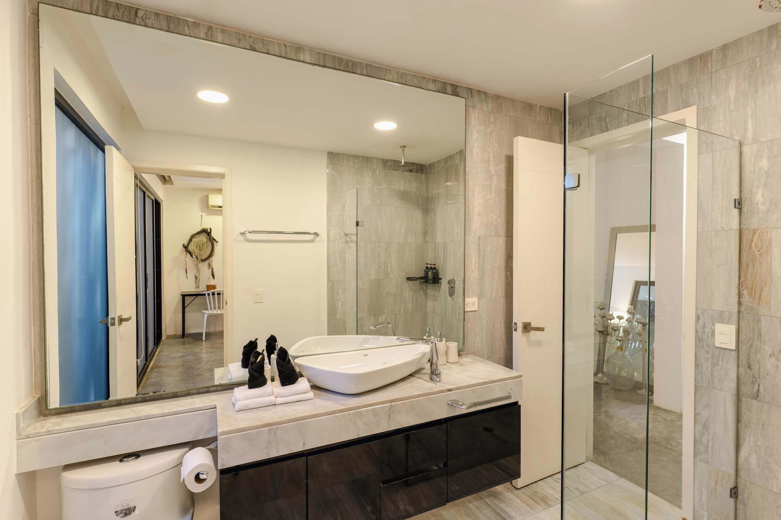 A modern bathroom with a large mirror, a double sink, a glass shower enclosure, and dark cabinetry.