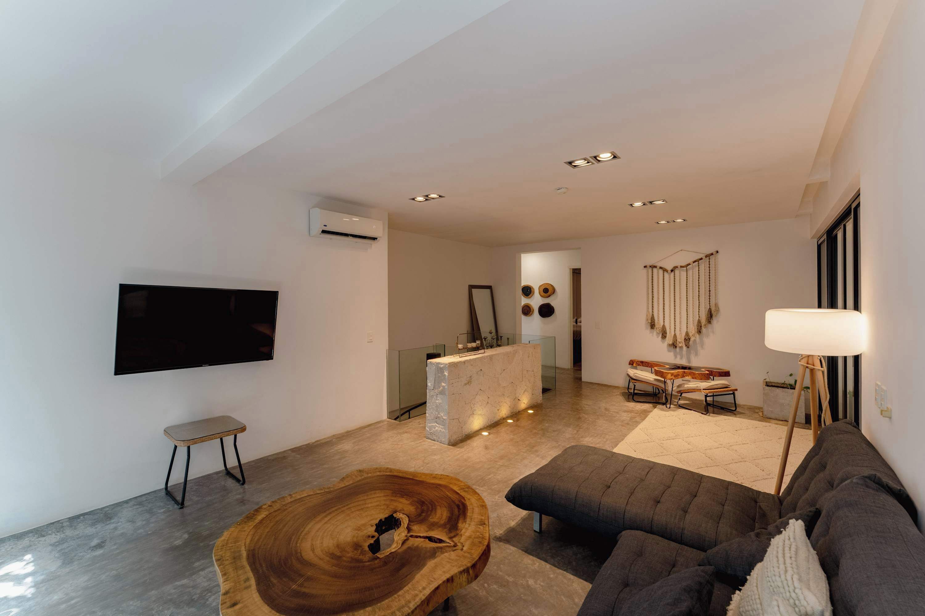 A modern living room with a flat-screen TV, a wooden coffee table, a gray sofa, a floor lamp, and a stone island with recessed lighting.