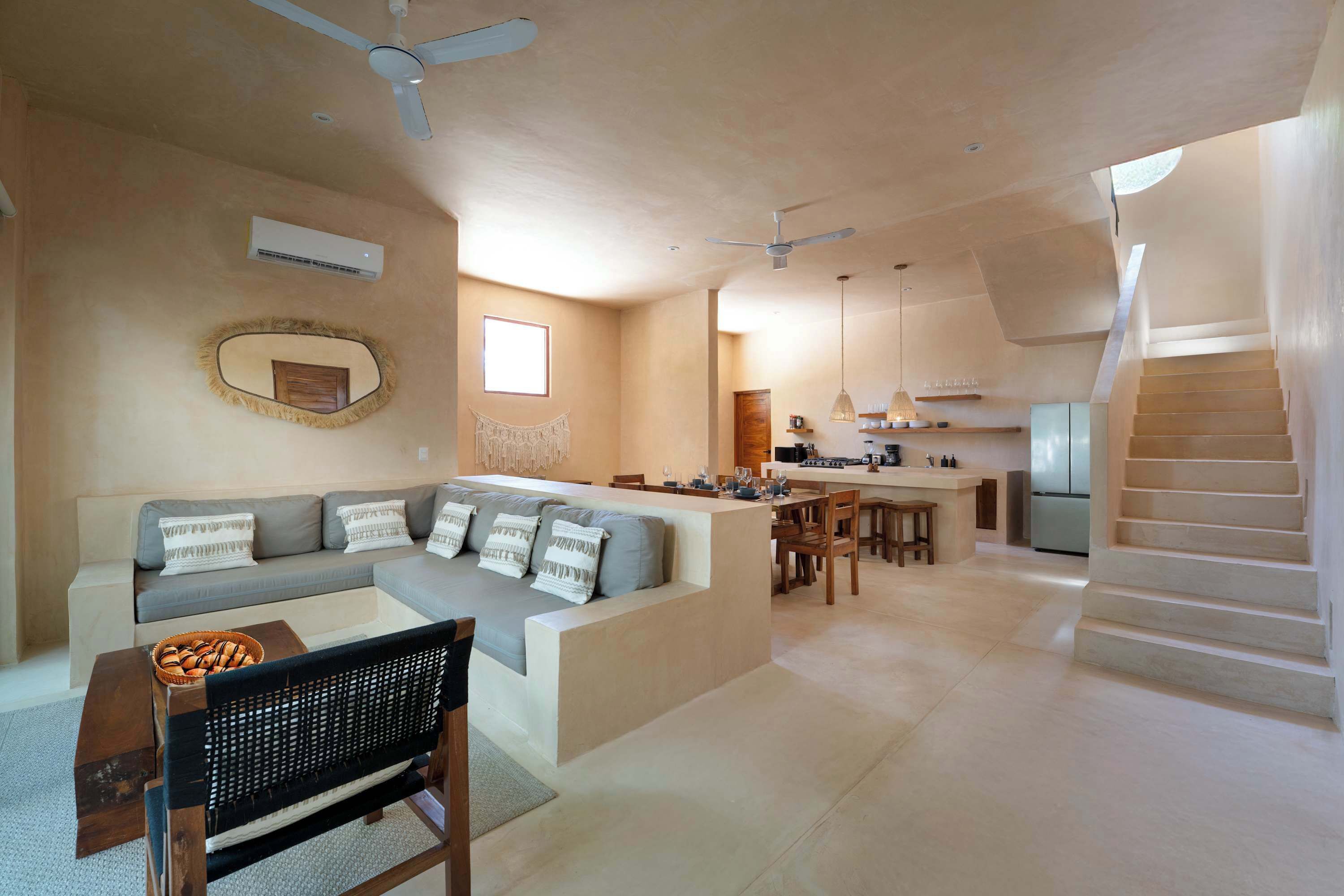 A modern living space with a sofa, dining area, kitchen, and a staircase.