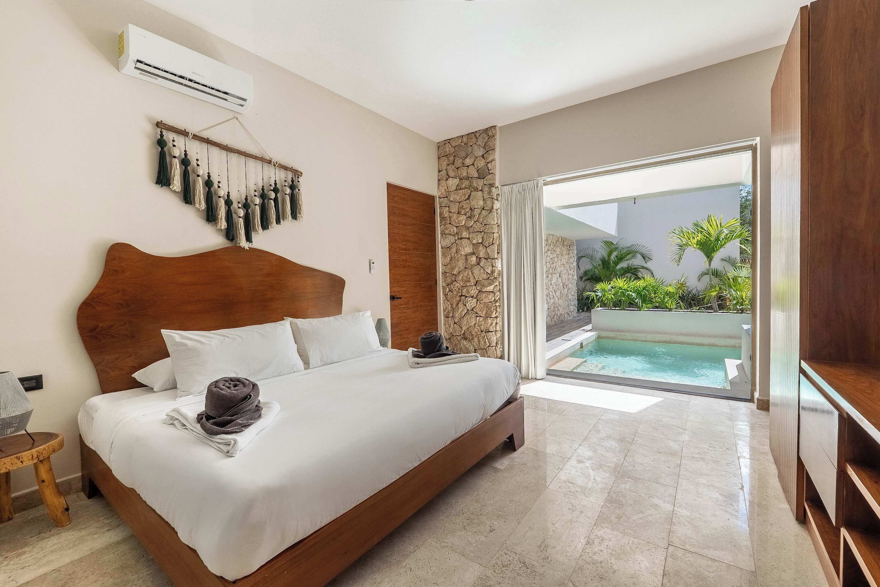 A bedroom with a large bed, a stone wall, a view of a swimming pool, and a sliding glass door.