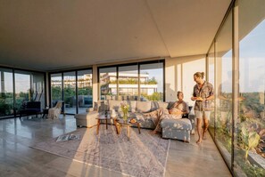 A modern living room with a sofa, coffee table, and large windows. - Spacious 2BR Jungle View w/ Private Pool & Balcony (Tulum)