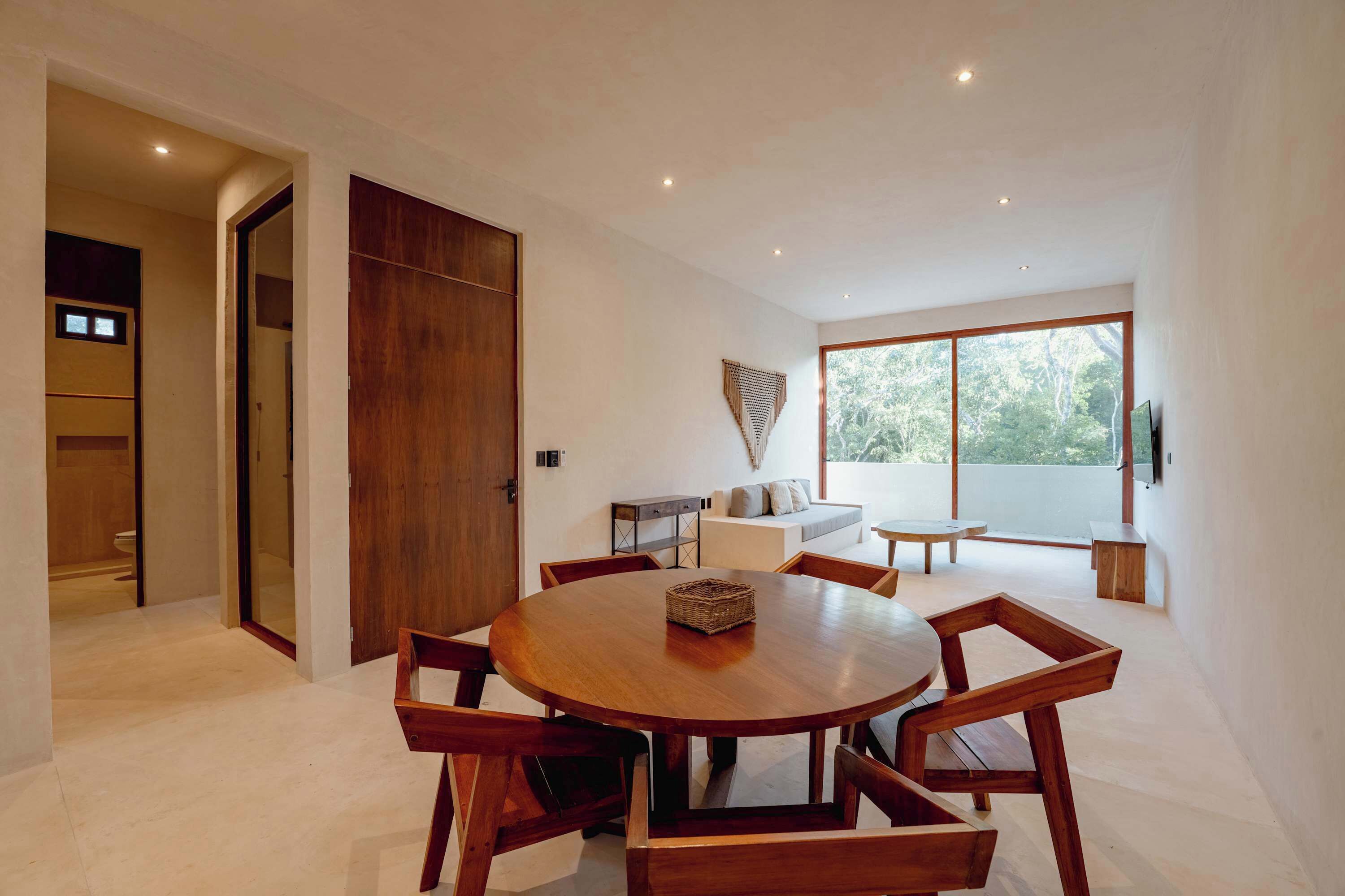 A modern dining area with a round wooden table and chairs, a sofa, and a large window with a view.