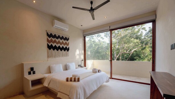 Un dormitorio con cama, ventilador de techo, ventana grande y aire acondicionado de pared.