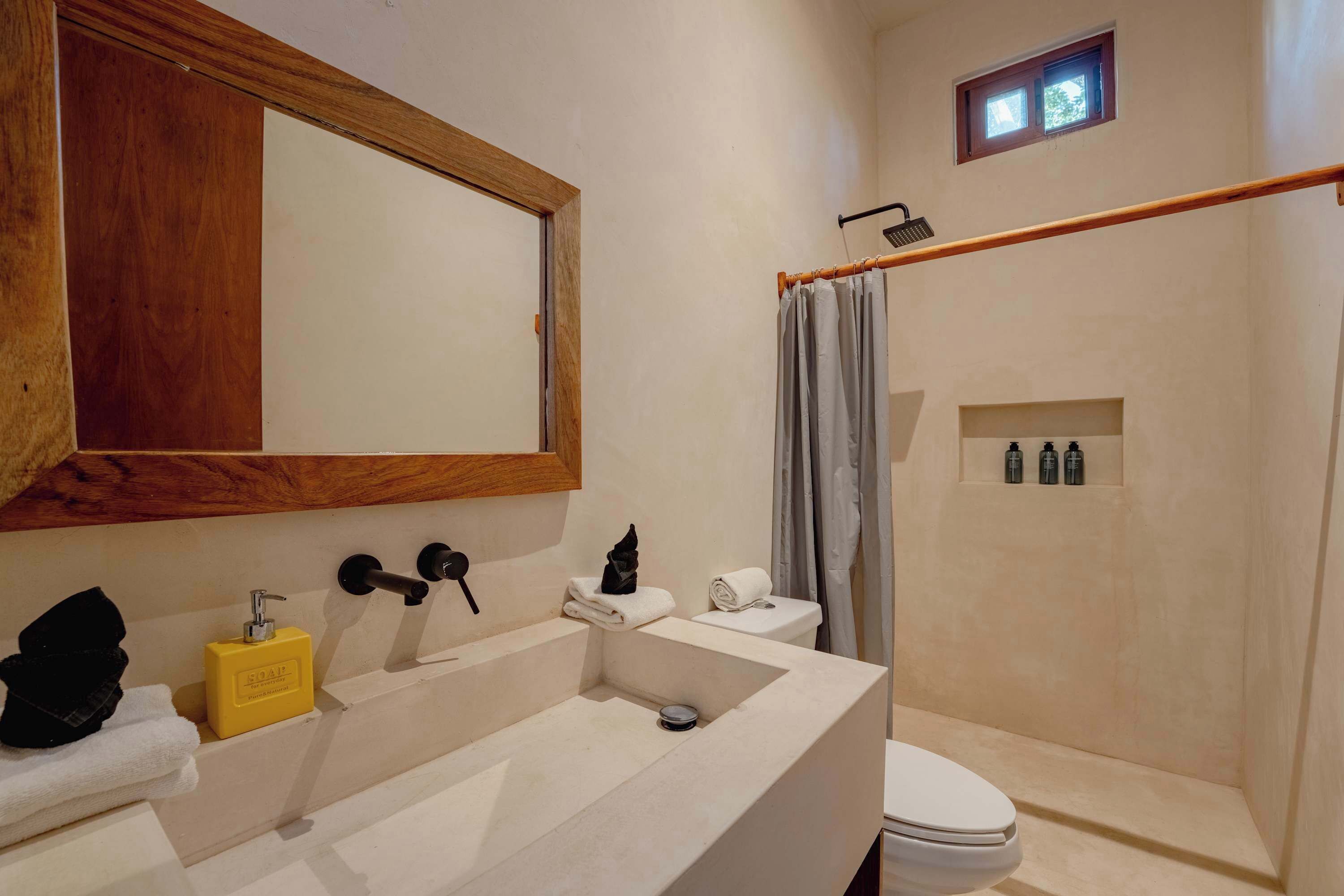 A bathroom with a wooden-framed mirror, a white sink, a toilet, and a shower area with a curtain.