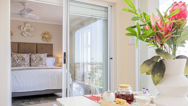 A bedroom with a bed, a sliding glass door to a balcony, and a breakfast tray on a table. - Bella View of Magestic Table Mountain (Cape Town)