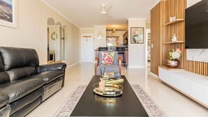 A living room with a black leather sofa, a coffee table with decorative items, a wooden TV stand, and a ceiling fan. - Bella View of Magestic Table Mountain (Cape Town)