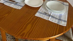 Une table de salle à manger ronde en bois, avec trois assiettes blanches et deux fourchettes posées sur des sets de table.