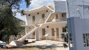 Un immeuble à plusieurs étages, à la façade blanche, avec un escalier doté d’une rampe en métal, et un arbre au premier plan.