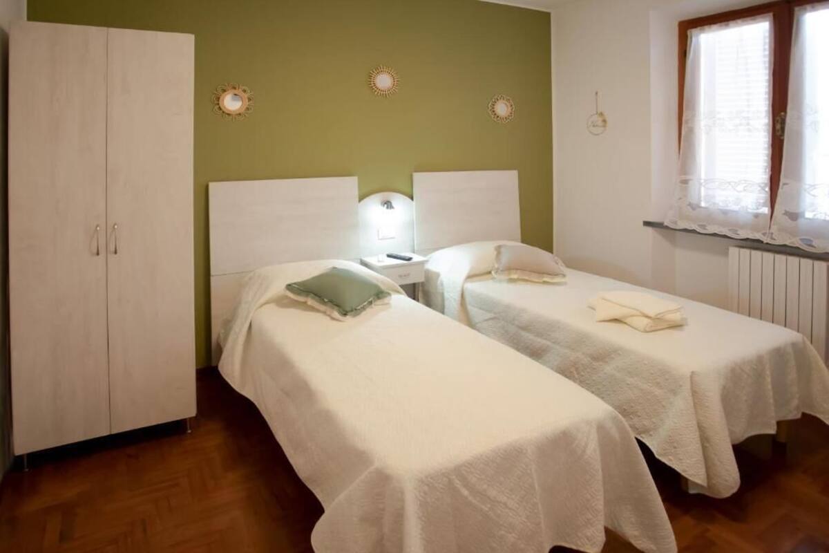 A room with two beds, a wardrobe, a nightstand, and a window with curtains.