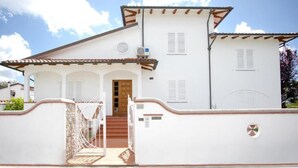 Un bâtiment blanc avec un toit recouvert de tuiles, une porte en bois et un petit porche doté d’une balustrade.