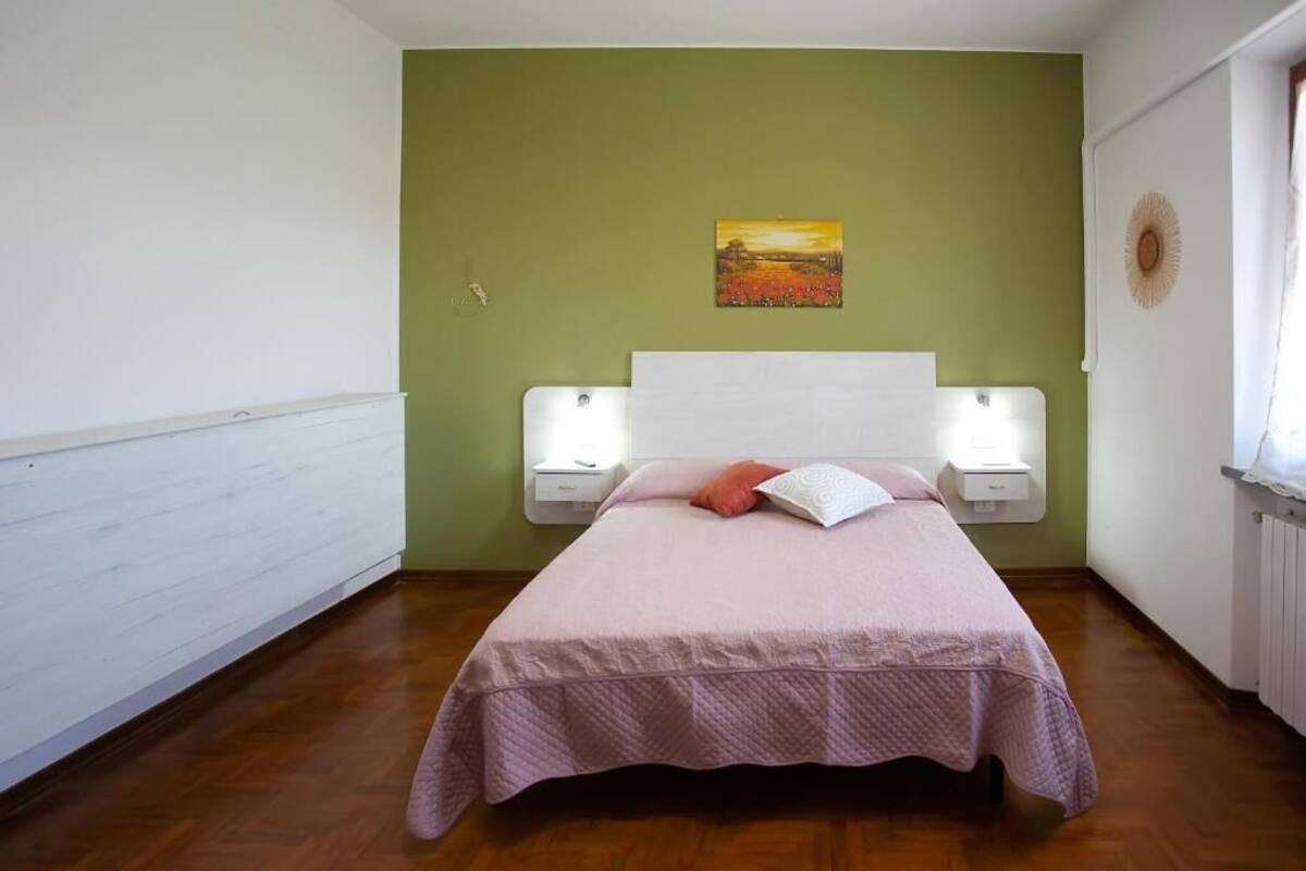 A bedroom with a bed, a nightstand, a wall-mounted lamp, and a painting.