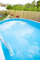 Una piscina con bordo in legno, un ombrellone bianco e una recinzione di legno.