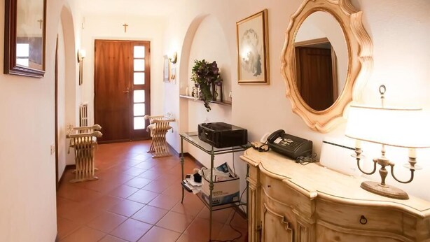 Un couloir avec une porte en bois, un radiateur, un bureau avec une lampe et un miroir.