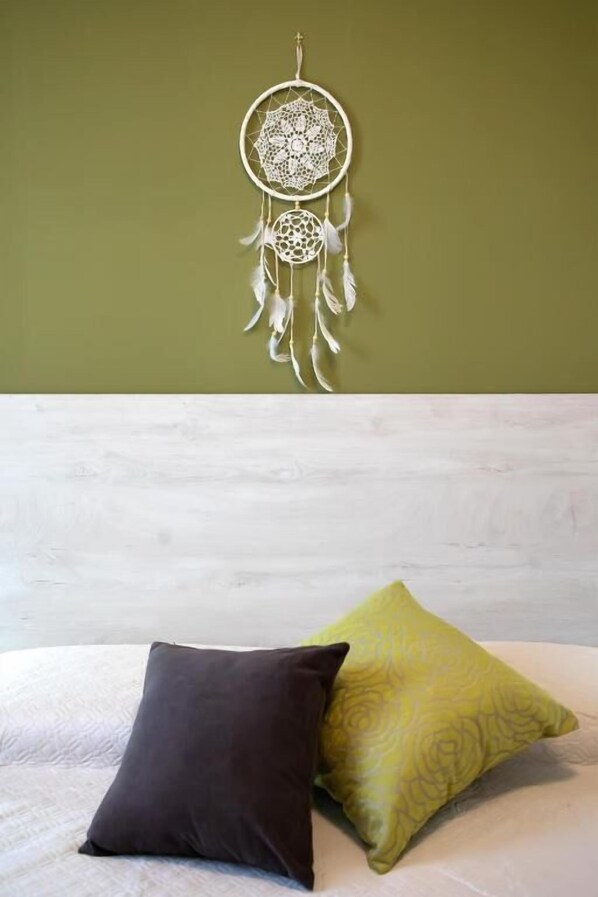 Una cama con dos almohadas, cabecera blanca y un atrapasueños colgado en la pared.