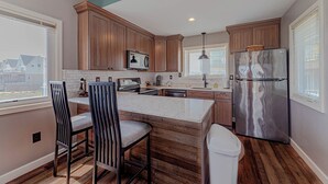 A kitchen with wooden cabinets, a stainless steel refrigerator, a marble countertop, and a view of houses outside. - JL #BR-9 - The Breakers 9 - Oceanfront - Community Pool (Kill Devil Hills)