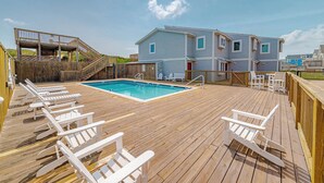 A wooden deck with a pool, white lounge chairs, and a two-story building with windows. - JL #BR-9 - The Breakers 9 - Oceanfront - Community Pool (Kill Devil Hills)