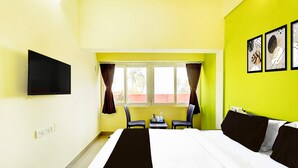 Una camera d'albergo con un letto, una TV a muro, una finestra con tende e un tavolo con sedie.
