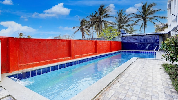 Piscina con parete rossa e piastrelle blu, circondata da palme e cielo sereno.