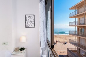 A room with a view of the beach, a bedside table with a lamp, a wall clock, and a framed picture. - Apartamentos Turisticos Rent Guardamar (Guardamar del Segura)