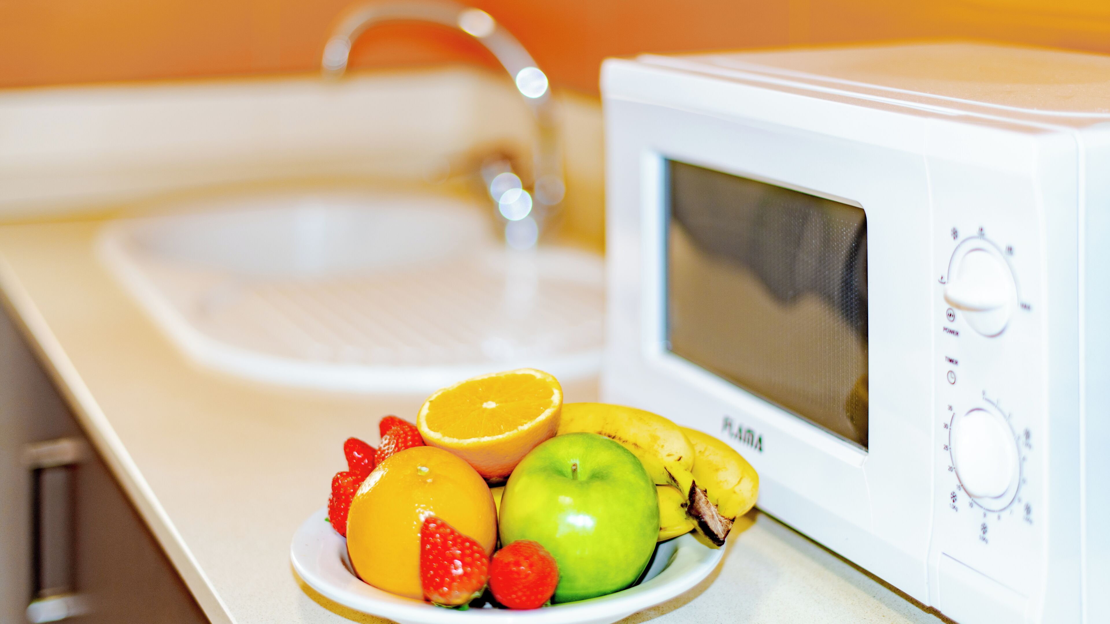 Una cocina con microondas, fregadero y un bol de fruta.