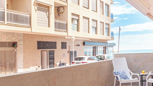 A balcony with a table set for two, a chair, and a view of the sea. - Apartamento Sirena (Guardamar del Segura)