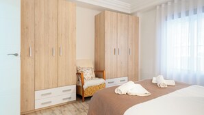 A hotel room with a bed, a chair, a wardrobe, and a window with curtains. - Apartamento Sirena (Guardamar del Segura)