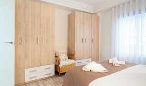 Ein Hotelzimmer mit Bett, Sessel, Schrank und einem Fenster mit Vorhängen.