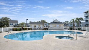 Una piscina con dos áreas separadas, rodeada por una valla blanca, con edificios y palmeras al fondo.