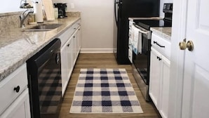 Una cocina compacta con gabinetes blancos, un refrigerador negro, un microondas y un lavavajillas.